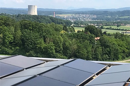 Blick über Hügel auf den Kühlturm eines Kernkraftwerks. Im Vorderrund sieht man einige Solarpanels.