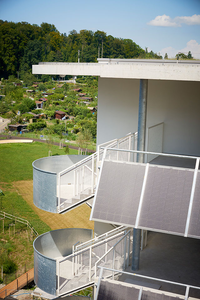 Seitliche Ansicht eines Wohngebäudes im Guggach III Quartier mit schräg gestellten Solarpanels und einem angrenzenden Grünbereich.