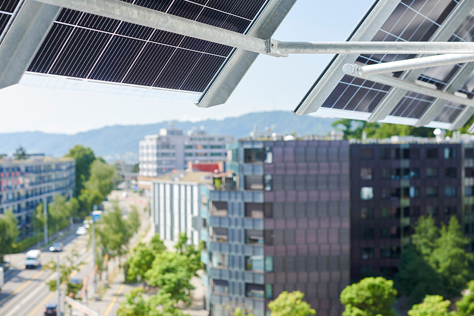 Solaranlagen auf einem Dach im Guggach III Quartier, mit Blick auf umliegende Gebäude und eine grüne Landschaft im Hintergrund.