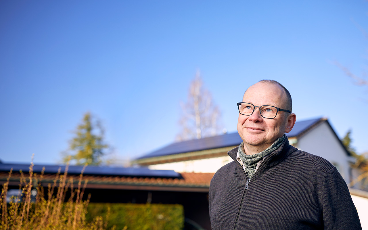 Mann steht vor seinem Haus. Auf dem Dach sind Solarmodule zu sehen