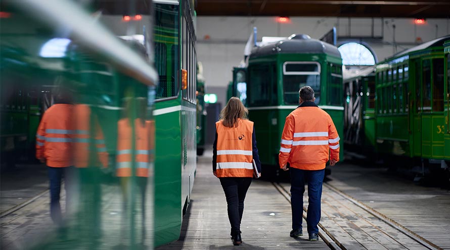 Zwei Mitarbeitende der Basler Verkehrsbetriebe in orangen Westen laufen auf ein Tram zu.
